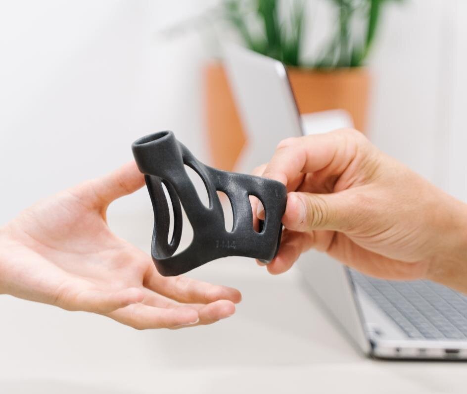Hand holding a custom 3D printed end-use part next to a laptop